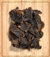 Pile of dark, dried meat pieces on a light wooden cutting board
