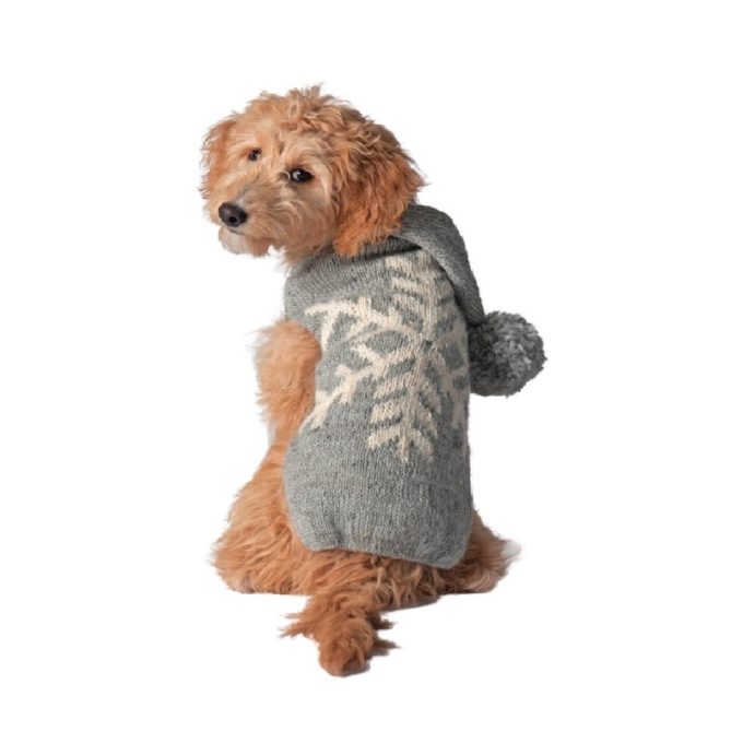A golden doodle dog wearing a gray knit sweater with a white snowflake pattern and a pom-pom on the hood