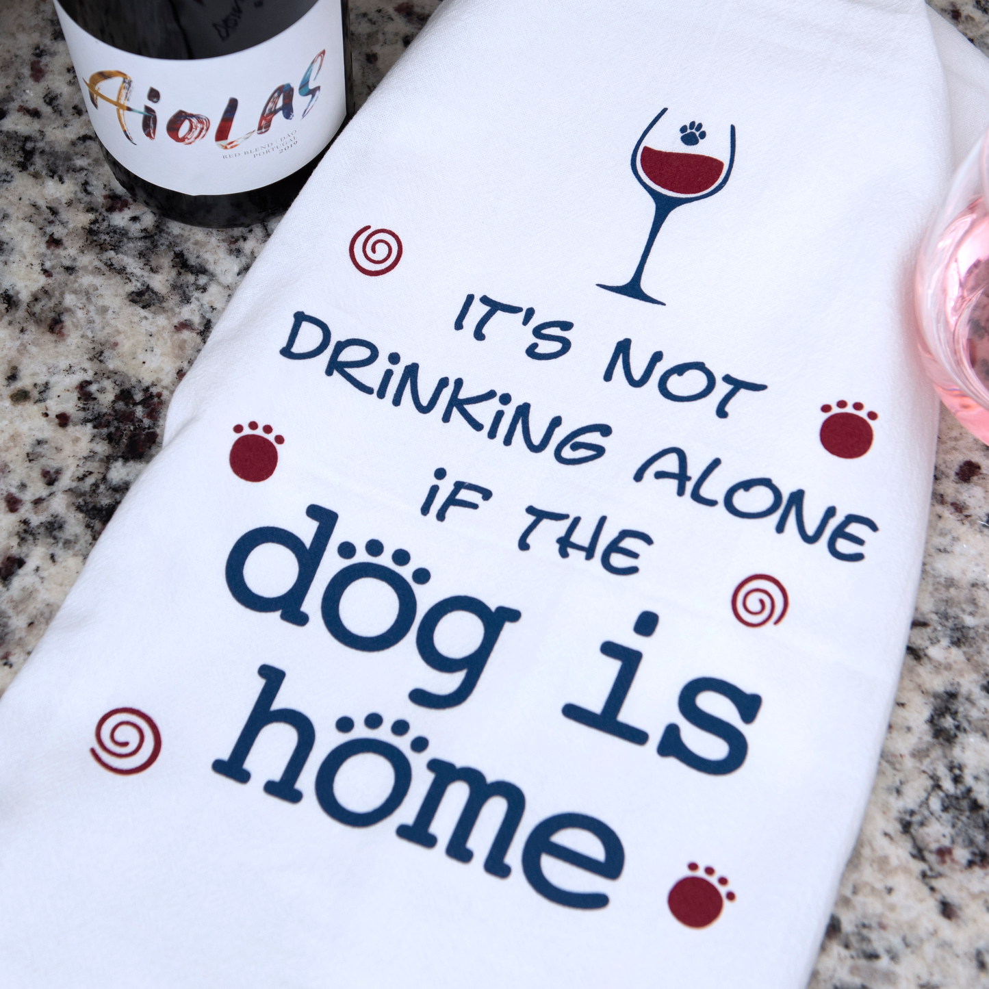 White tea towel with a wine glass and paw print graphic and the text It's not drinking alone if the dog is home