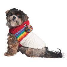 Small dog wearing a red, rainbow, and white knitted sweater with a pom-pom on the hood